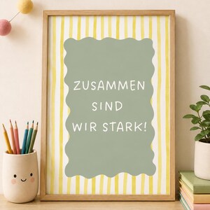 Könnte beinhalten: Ein gerahmtes Wandbild mit einem hellgrünen, gewellten Rechteck auf einem Hintergrund mit gelben und weißen vertikalen Streifen. Der Text ZUSAMMEN SIND WIR STARK! ist in weißen Großbuchstaben innerhalb der grünen Form abgedruckt.