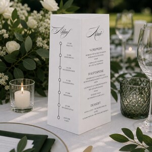 May include: A white, three-sided wedding menu card with elegant script. The menu lists a timeline and meal options. The card is on a table set with white roses, candles, and gold-rimmed plates. A formal event setting.