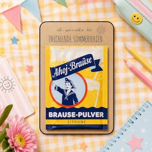 Könnte beinhalten: Eine rechteckige Karte mit dem Text 'ich wünsche dir PRICKELNDE SOMMERFERIEN' und einem gelben Ahoj-Brause Zitronen-Brausepulver-Tütchen. Das Tütchen zeigt eine Matrosen-Illustration, ein Glas Brause und den Text 'Ahoj-Brause' sowie 'BRAUSE-PULVER ZITRONE'.