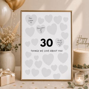 May include: A vertical rectangular poster in a gold frame featuring the large black number 30 and the text THINGS WE LOVE ABOUT YOU. The design includes multiple light grey heart shapes, some containing German text and small heart icons.
