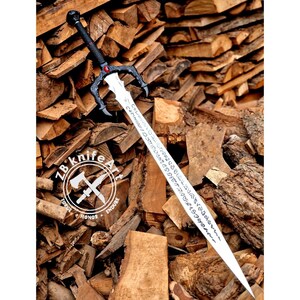 May include: A long, silver sword with a black handle and guard, featuring intricate designs and inscriptions on the blade. The sword has a red gem at the center of the guard and a skull at the pommel. The sword is displayed against a backdrop of stacked firewood.