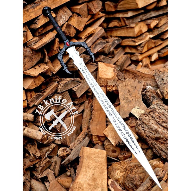 May include: A long, silver sword with a black handle and guard, featuring intricate designs and inscriptions on the blade. The sword has a red gem at the center of the guard and a skull at the pommel. The sword is displayed against a backdrop of stacked firewood.