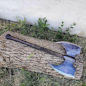 May include: A double-bit battle axe featuring a long, dark brown wooden handle and a large, wide metal axe head with a textured, weathered finish. The axe head has two symmetrical, curved blades extending from a central reinforced metal collar.