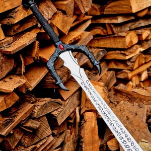 May include: A detailed sword with a black handle and guard, featuring a red gem. The blade is silver with etched inscriptions. The sword rests against a backdrop of stacked firewood, showcasing a rustic aesthetic.
