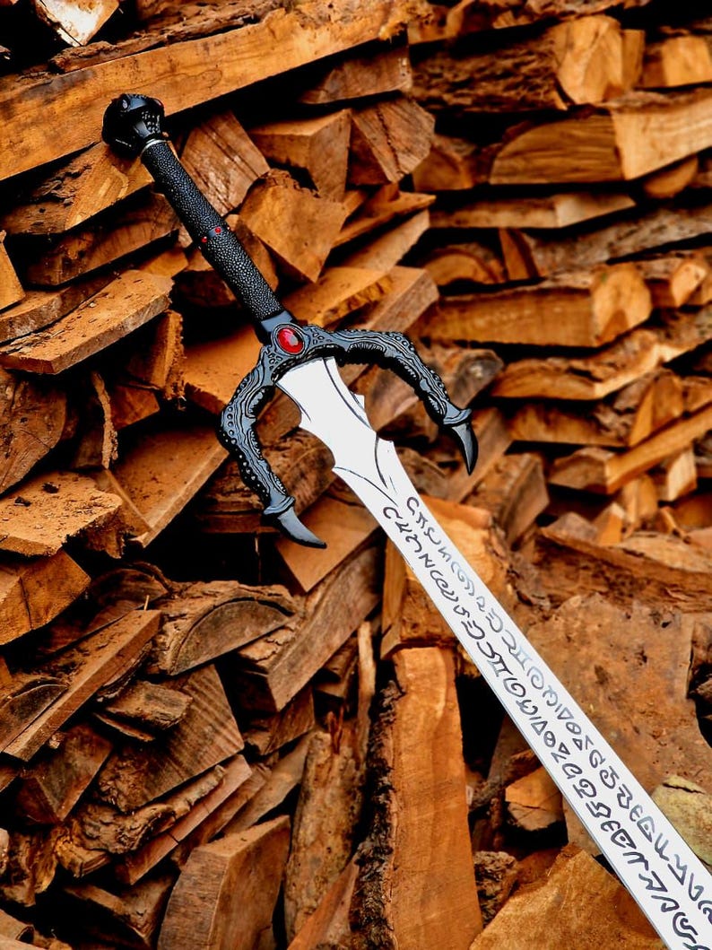 May include: A detailed sword with a black handle and guard, featuring a red gem. The blade is silver with etched inscriptions. The sword rests against a backdrop of stacked firewood, showcasing a rustic aesthetic.