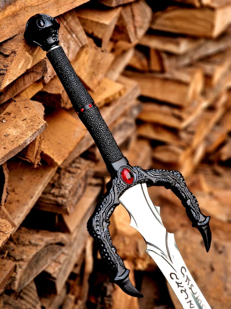 May include: A decorative sword with a black handle and guard, featuring a skull-shaped pommel. The blade is silver with etched designs. A red gem is set in the guard. The sword is leaning against a stack of wood.