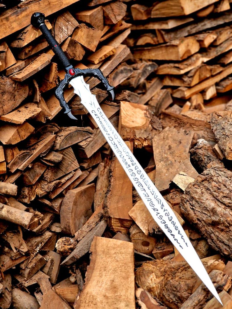 May include: A decorative sword with a black handle and guard, featuring a red gem and ornate detailing. The silver blade has etched inscriptions. The sword rests against a backdrop of stacked firewood, creating a rustic aesthetic.