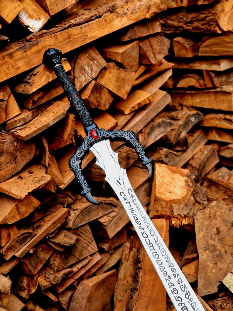 May include: A detailed fantasy sword with a black handle and guard, featuring a red gem and intricate designs. The silver blade has engraved text. The sword is set against a backdrop of stacked firewood.
