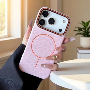 May include: A light pink phone case with a textured leather-like finish. The case has a circular design with an orange outline and a matching orange line. The camera area has an orange border.