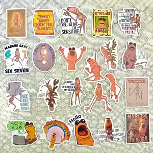 May include: A collection of colorful stickers featuring cartoon characters with various expressions and text. The stickers include phrases like "Jimbo James Took The Snacks," "I'm Lost," and "Marcus Says Six Seven." The stickers are on a white lace surface.