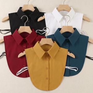 Peut inclure: Cinq cols de chemise amovibles en noir, blanc, bordeaux, jaune moutarde et bleu sarcelle, chacun avec un devant boutonné. Les cols sont présentés sur des cintres en bois.