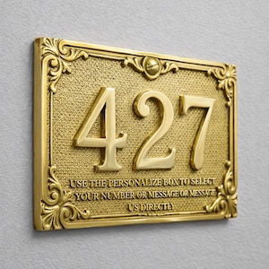 Może przedstawiać: Prostokątna mosiężna tablica z numerem domu "427" z wypukłymi literami. Tablica ma ozdobną obwódkę i tekst "USE THE PERSONALIZE BOX TO SELECT YOUR NUMBER OR MESSAGE OR MESSAGE US DIRECTLY".
