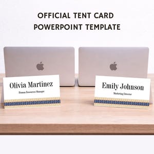 May include: Two white tent cards with names and titles, "Olivia Martinez, Human Resources Manager" and "Emily Johnson, Marketing Director", sit on a wooden surface. Each card has a decorative blue and tan ribbon. Two silver laptops are in the background.