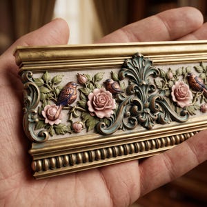 May include: A rectangular decorative molding piece featuring an ornate relief design. The gold-toned frame contains sculpted pink roses, green leaves, and small brown birds. The border includes a beaded edge detail and intricate scrollwork.
