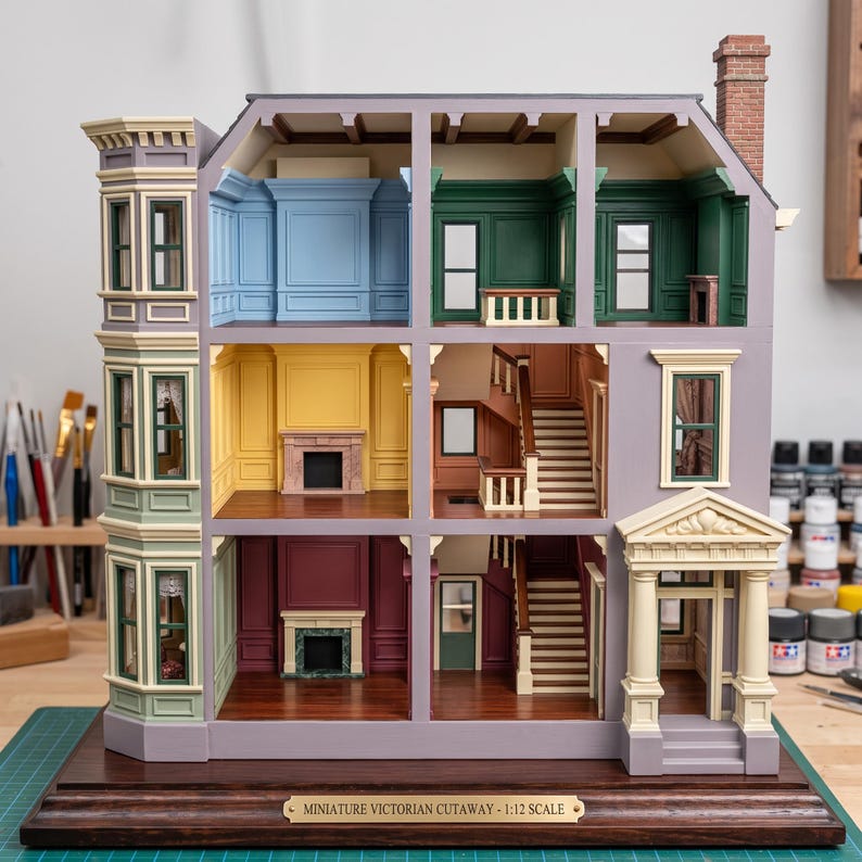 May include: A 1:12 scale miniature Victorian cutaway dollhouse featuring three levels of rooms with distinct wall colors including blue, green, yellow, and maroon. The structure includes a front entrance, staircases, and a plaque reading Miniature Victorian Cutaway - 1:12 Scale.