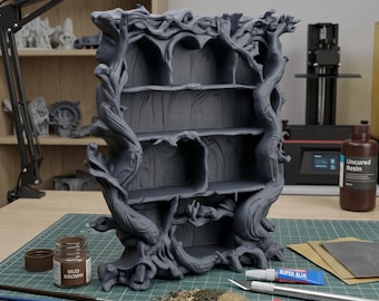 Può includere: Una libreria grigia a forma di albero con più ripiani. La libreria è progettata in modo intricato con un'estetica naturale e organica. Varie forniture per l'artigianato, tra cui vernice, pennelli e colla, sono disposte su un tappetino da taglio verde.
