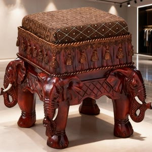May include: A decorative wooden stool with a dark brown finish, featuring carved elephant legs and a cushioned top. The cushion is a patterned brown fabric. The stool has a detailed design with tassels and rope accents, adding to its ornate appearance.