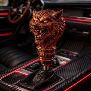 May include: A detailed wooden shift knob featuring a snarling wolf head with glowing yellow eyes. The knob is intricately carved and mounted on a black leather shift boot. The interior of the car has red accent lighting.