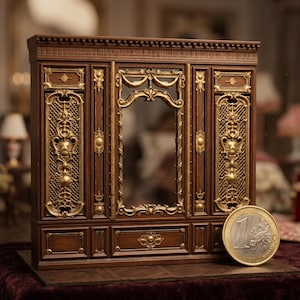 May include: A miniature dark wood wall panel featuring intricate gold-colored metal filigree accents, a central rectangular mirror, and decorative molding. A 1 Euro coin is placed in the foreground to provide a clear sense of scale for the piece.