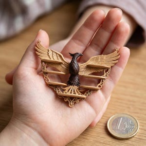 以下が含まれることがあります： 羽を広げたフェニックスの木彫りの彫刻。鳥は茶色で、翼はタン色で、手に持たれています。彫刻は複雑なディテールがあり、装飾品のように見えます。