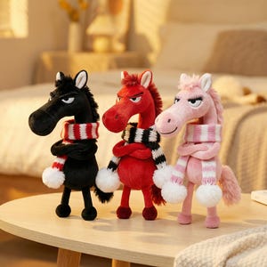 May include: Three plush horse figures in black, red, and pink, each wearing a scarf with white pom-poms. The black horse has a red and white striped scarf, the red horse has a black and white striped scarf, and the pink horse has a pink and white striped scarf.