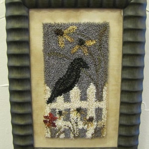 May include: A framed needlepoint artwork depicting a black crow perched on a white picket fence with yellow flowers in the background.