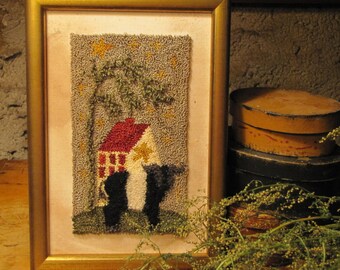 May include: A framed needlepoint artwork depicting a small white house with a red roof, a tree, and two black cats under a starry night sky.