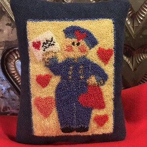 May include: A decorative pillow with a navy blue border and a central design featuring a postal worker holding a letter with a heart. The background is yellow, with red hearts scattered around the image.