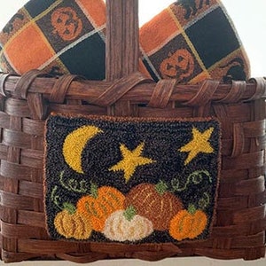 Puede incluir: Una cesta de mimbre marrón con dos toallas de cuadros naranja y negro y una pequeña pieza de punto de aguja con una luna, estrellas y calabazas. La pieza de punto de aguja dice "Happy Fall".
