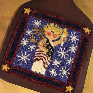 May include: A needlepoint wall hanging featuring a blue background with a white figure holding a golden star. The figure is wearing a red, white and blue striped outfit. The background is decorated with white snowflakes.