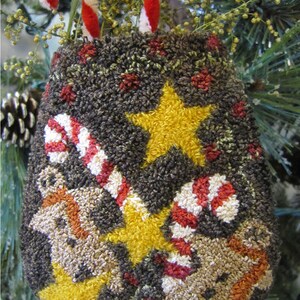 May include: A brown felt Christmas bauble featuring a candy cane, stars, and gingerbread men design. The bauble is decorated with red, white, and yellow yarn.