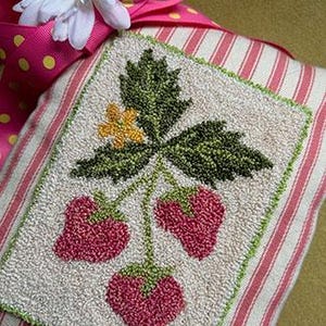 Puede incluir: Una almohada de punto de aguja hecha a mano con un tallo verde frondoso con tres fresas rosas. La almohada está hecha con una tela blanca con rayas rosas y blancas.