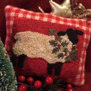 Peut inclure: Un coussin en plaid rouge et blanc avec un mouton blanc tenant une couronne de houx verte. Le mouton a un visage noir et des pattes noires. Le coussin est décoré d'une étoile dorée et d'un ruban doré.