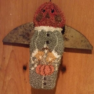 May include: A gray and red felt snowman ornament with a white felt hat and a brown felt nose. The snowman is hanging from a rusty metal hook.