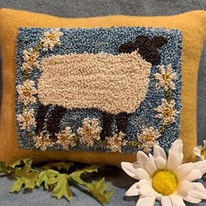 May include: A yellow wool pillow with a blue and white needlepoint design of a white sheep with black legs and head surrounded by white daisies.