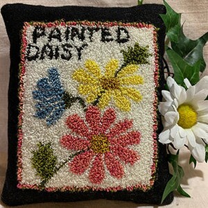 May include: A black felt pillow with a hand-stitched design of three colorful daisies and the text "PAINTED DAISY".