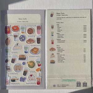 May include: A clear plastic sleeve with stickers and a menu. The stickers depict drinks and pastries, such as iced matcha, strawberry lemonade, and sandwiches. The menu lists drinks and sweets available at the Home Cafe.