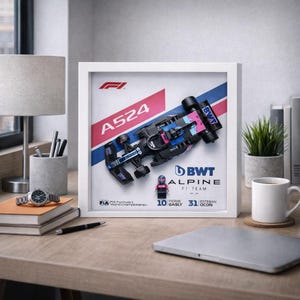 May include: A framed LEGO model of an Alpine F1 race car, with black, blue, and pink details. The frame displays "A524" and "BWT Alpine F1 Team." A small LEGO figure of a driver is also included.