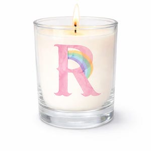 May include: A lit, white candle in a clear glass jar. The candle has a pink letter "R" with a rainbow design. The candle is on a white background.