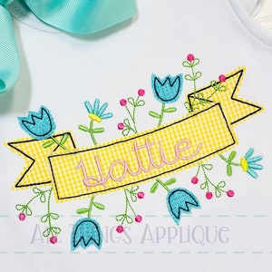 May include: A yellow and white gingham banner with the name "Hattie" embroidered in pink. The banner is surrounded by blue and yellow flowers with green stems and pink berries.