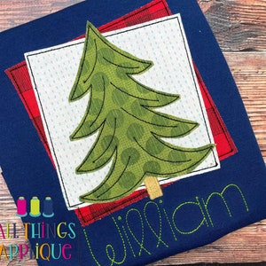 Könnte beinhalten: Ein blauer Stoff mit einer grünen und braunen Baum-Applikation in einem weißen Quadrat mit einem roten und weißen karierten Rand. Der Name "William" ist in grünem Garn unter dem Baum gestickt.