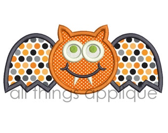 Puede incluir: Aplique de murciélago naranja y negro con una cara sonriente y colmillos. El murciélago tiene alas con lunares.
