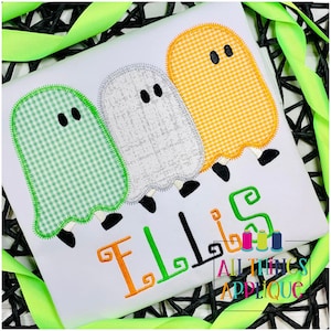 May include: A white t-shirt with three embroidered ghosts in green, white, and orange gingham patterns. The ghosts have black eyes and feet. The name "Ellis" is embroidered in orange, green, and black letters below the ghosts.