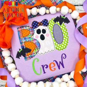 May include: Purple shirt with a colorful applique of the word "BOO" with a ghost and bats. The word "Crew" is embroidered below the applique.