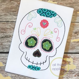 May include: Embroidered sugar skull design with black outlines, green and teal flowers, and pink hearts. The skull is white with a black nose and mouth.