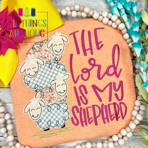 May include: A peach-colored t-shirt with a pink embroidered design of four stacked sheep and the text "The Lord is My Shepherd".