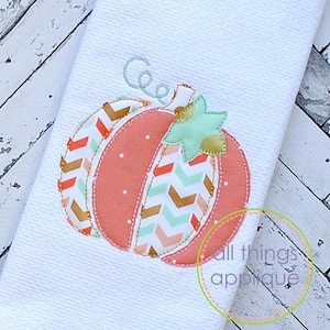 May include: A pink and orange pumpkin applique with a chevron pattern and a green leaf. The applique is stitched with a light brown thread and has the name "Coe" embroidered above it. The applique is on a white background.