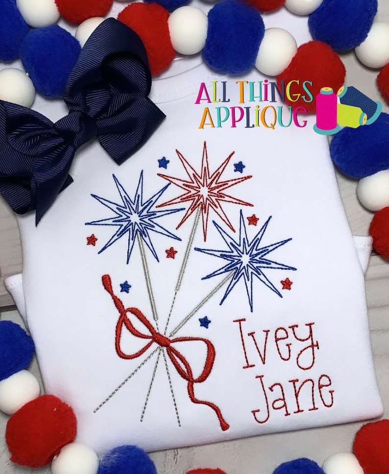 May include: White t-shirt with red, white, and blue embroidered fireworks and a red bow. The name "Ivey Jane" is embroidered below the fireworks. The text "All Things Applique" is in the top right corner of the image.
