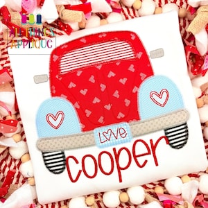 May include: White t-shirt featuring a red truck design with white hearts. The truck has light blue fenders with heart details and the word "Love" on the license plate. The name "Cooper" is embroidered in red.