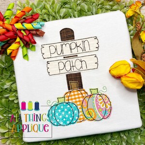 Könnte beinhalten: Ein weißes Shirt mit einem gestickten Design eines Holzschildes, auf dem "pumpkin patch" steht, und drei Kürbissen darunter. Die Kürbisse haben verschiedene Muster: einer ist kariert, einer ist gepunktet und einer ist Paisley.